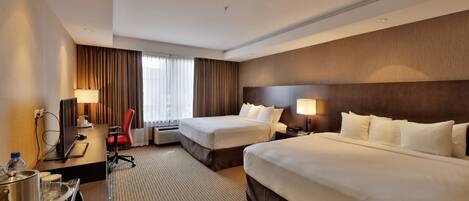 A hotel room with two beds, a desk with a computer, a chair, and a large window with curtains.