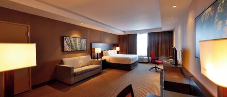 A hotel room with a bed, a sofa, a desk, and a TV.