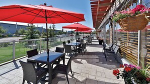 Una terraza con mesas y sillas, sombrillas rojas y macetas colgantes de flores.