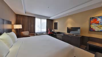Una habitación de hotel con una cama grande, un escritorio, una silla, un televisor y un cuadro en la pared.