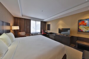 Una habitación de hotel con una cama grande, un escritorio, una silla, un televisor y un cuadro en la pared.