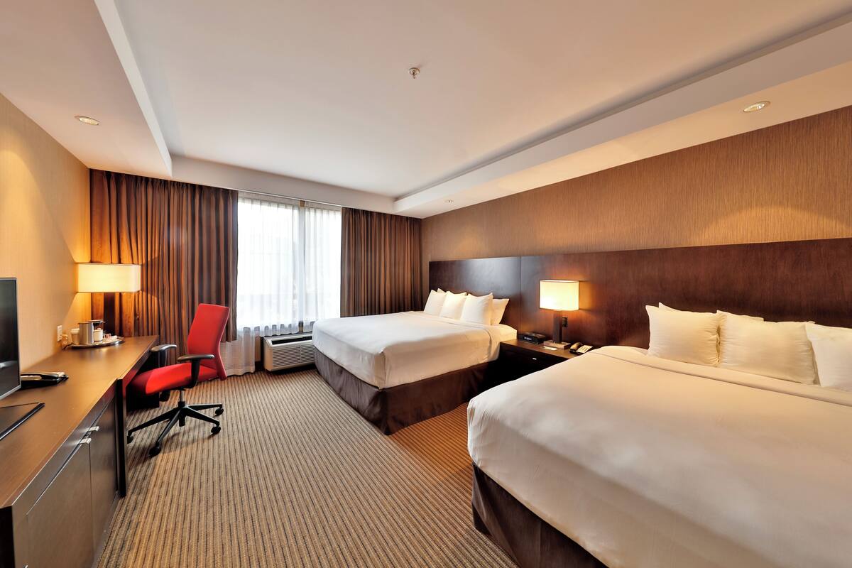 A hotel room with two beds, a desk, a chair, and a TV.