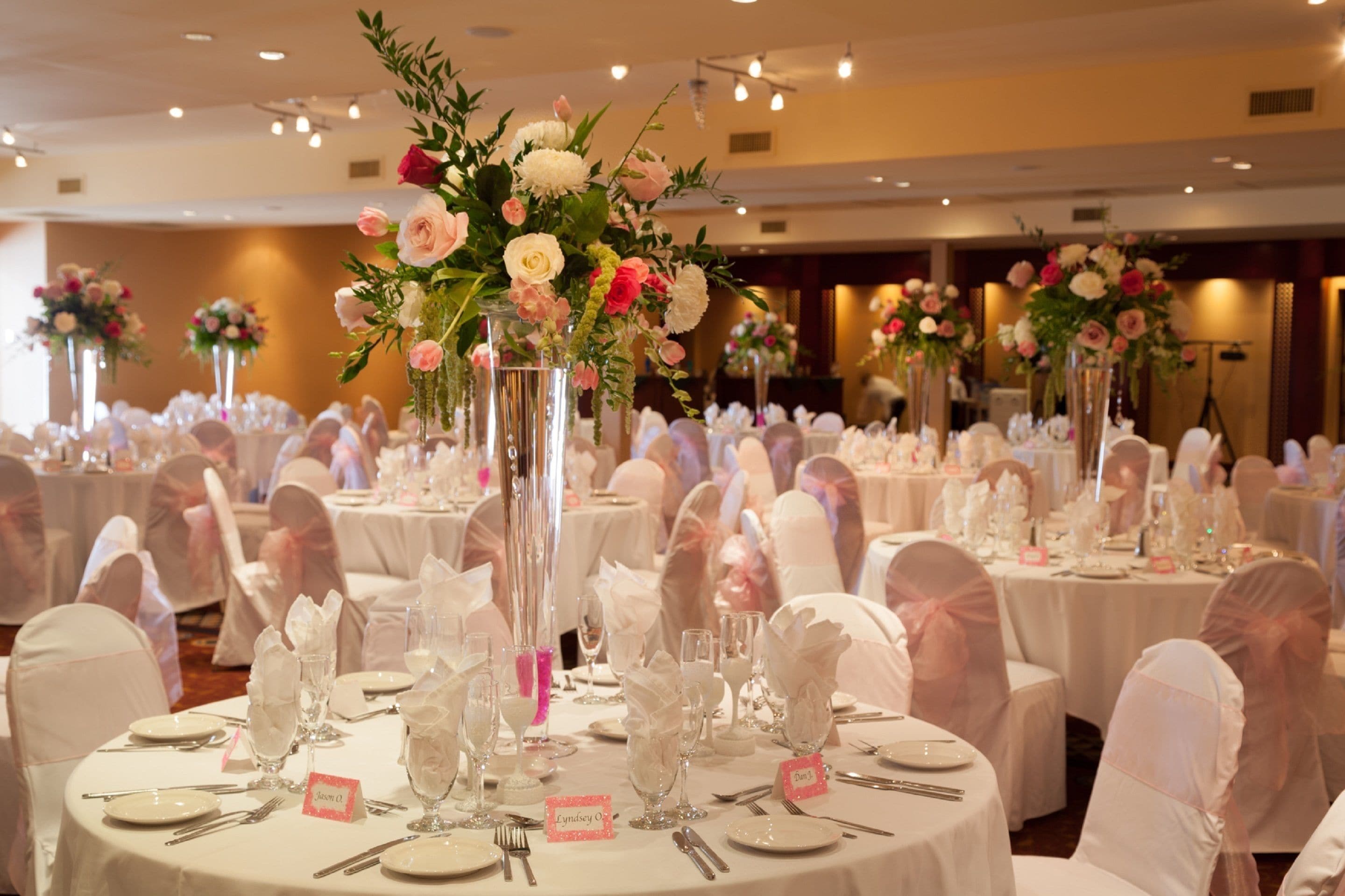A banquet hall with round tables set for a formal event, each with a name card, glassware, and white tablecloths.