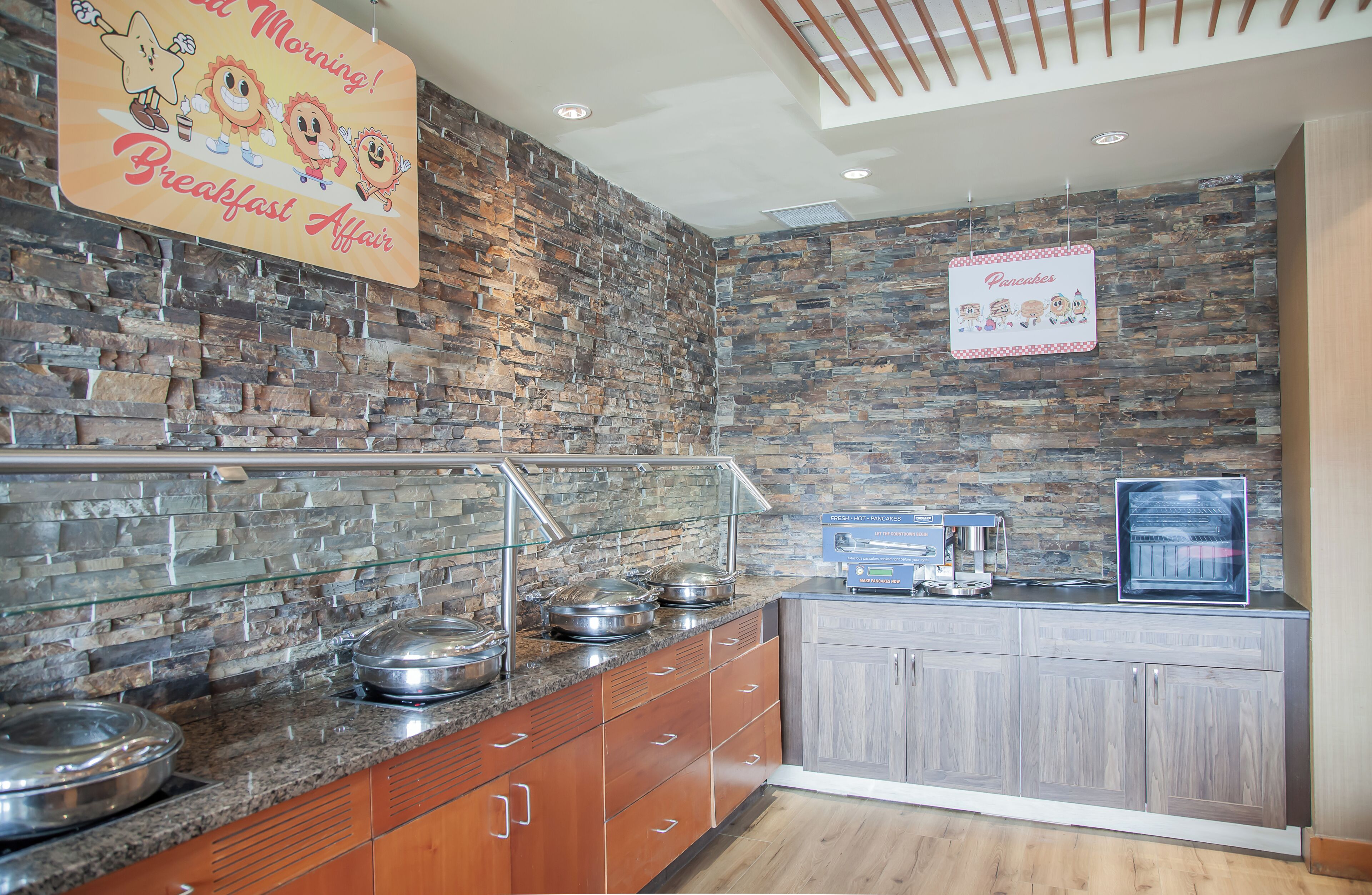 A breakfast area with a stone wall, buffet with food containers, and a sign indicating breakfast service.