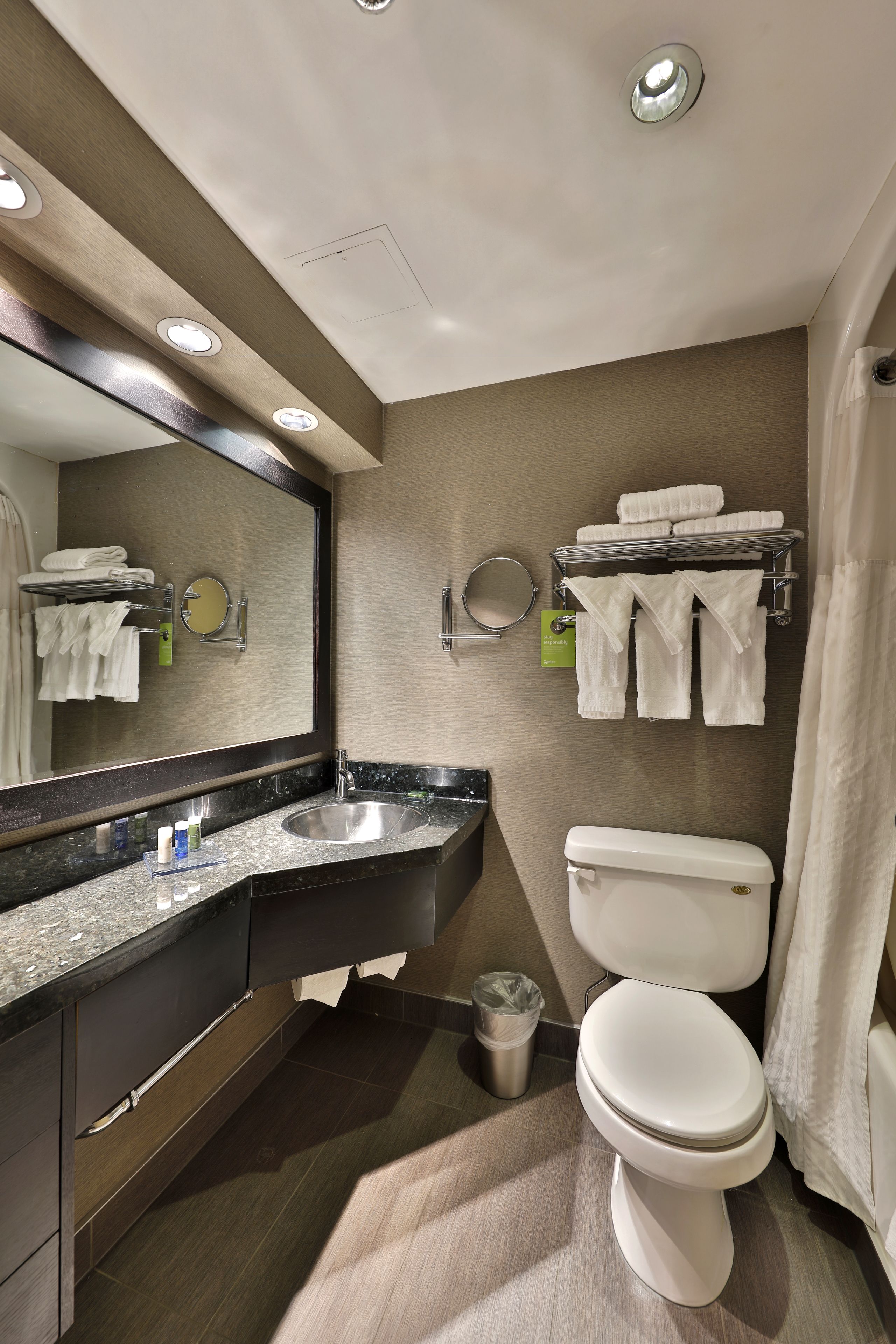 A modern bathroom with a large mirror, a sink, a toilet, and towel racks.