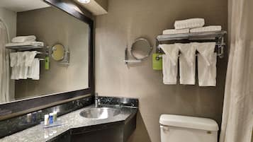 A modern bathroom with a large mirror, a sink, a toilet, and towel racks.