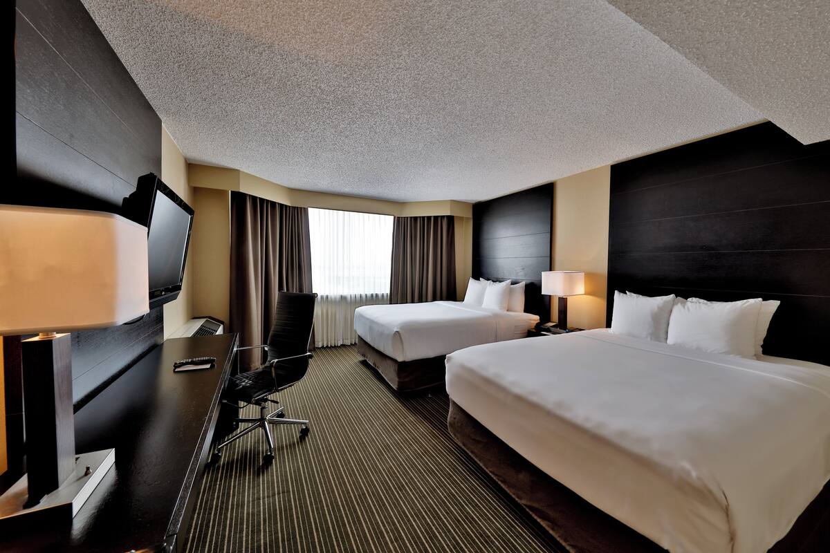 A hotel room with two beds, a desk with a computer, a TV, and a window with curtains.