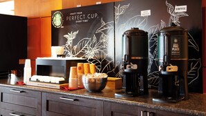 Una estación de café con una cafetera, un recipiente de café Starbucks Pike Place Medium Roast y un portavasos.