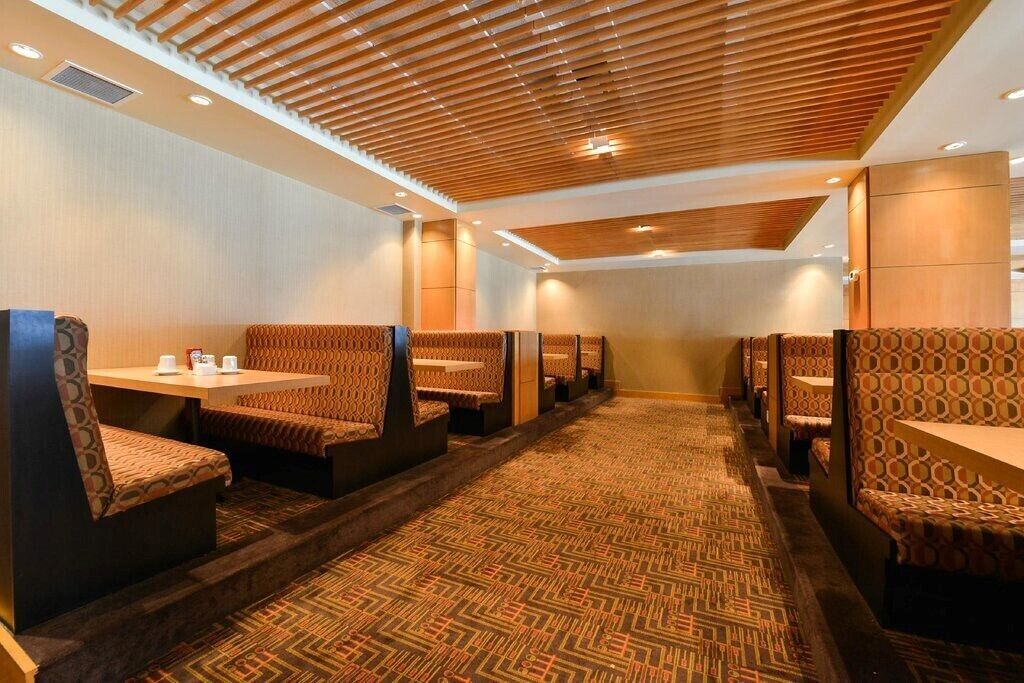A hotel lobby with patterned carpet, wooden ceiling, and seating areas with tables and chairs.