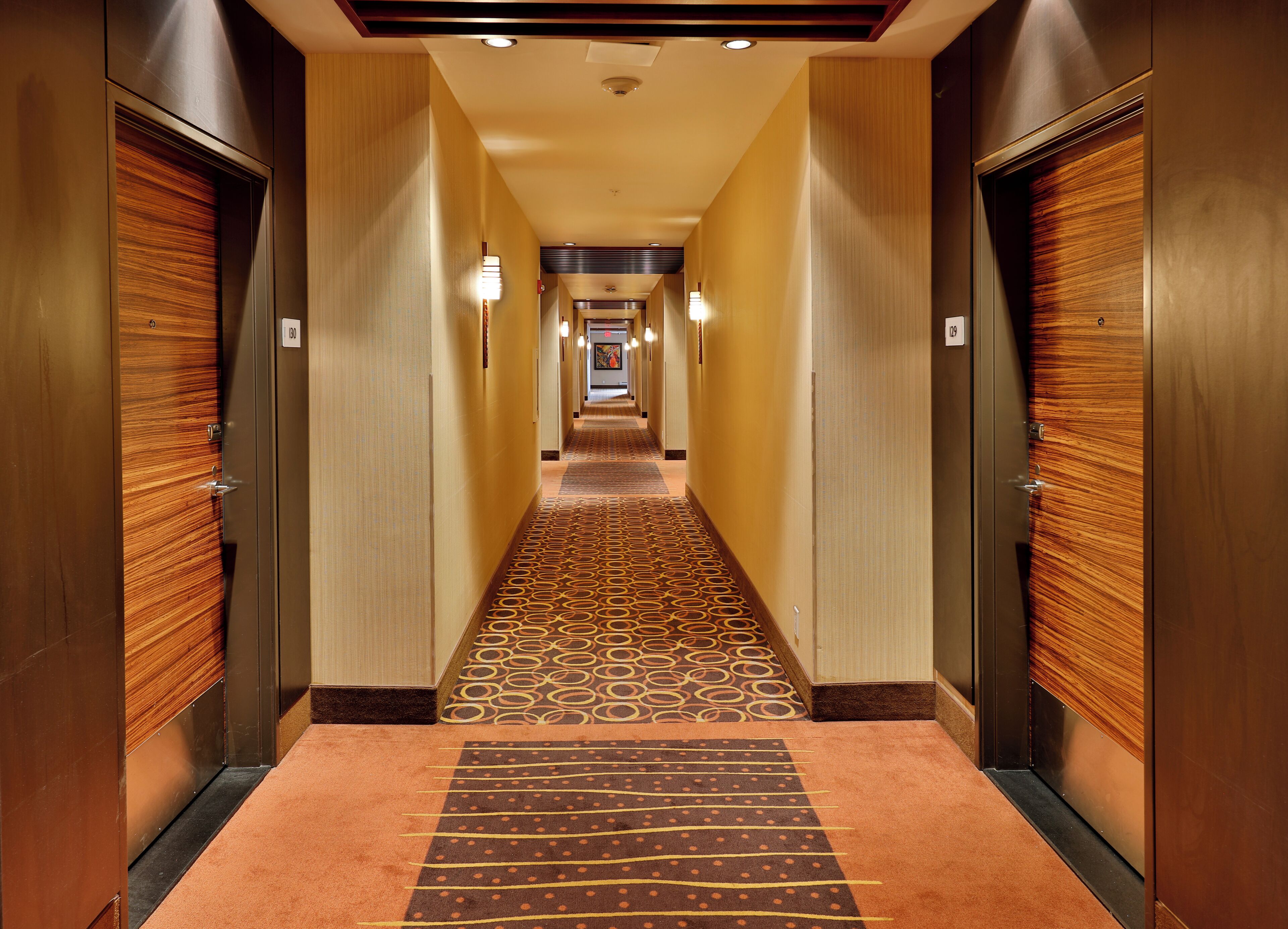 A hotel hallway with wooden doors, a patterned carpet, and a light-colored wall.