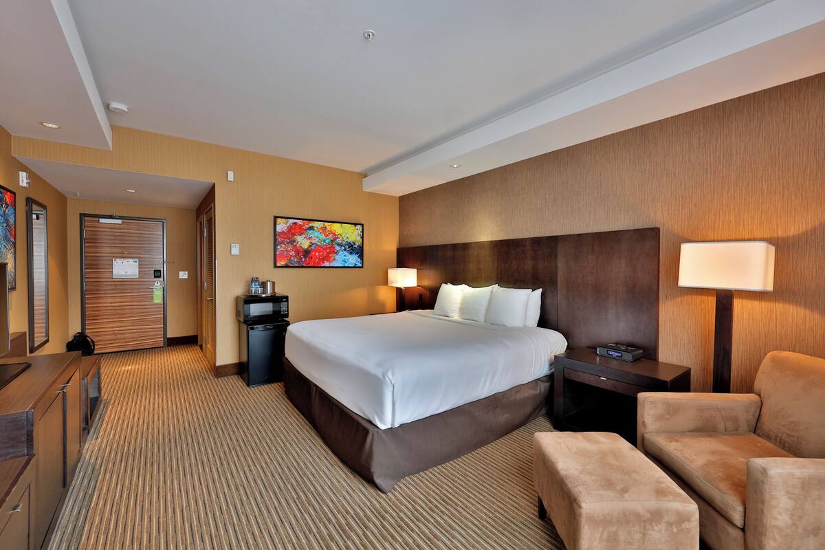 A hotel room with a large bed, a desk, a chair, a nightstand, and a wall-mounted TV.