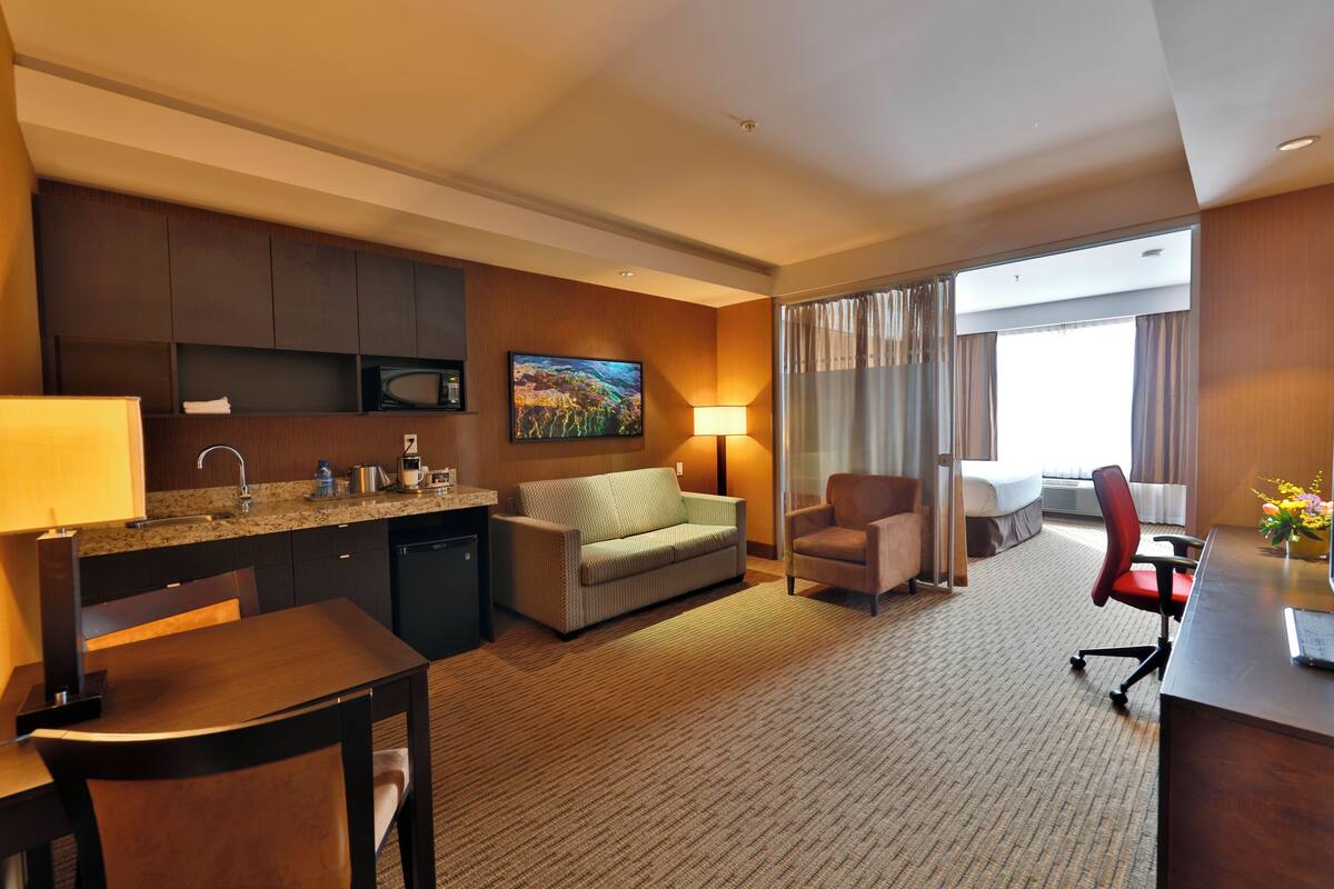 A hotel room with a kitchenette, a sofa, a desk, and a chair.