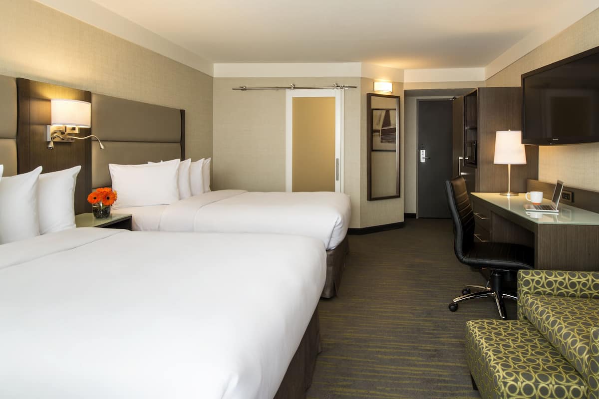 A hotel room with two beds, a desk, a chair, a TV, and a mirror.