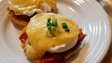 A plate with two eggs benedict sandwiches topped with hollandaise sauce and garnished with chives.