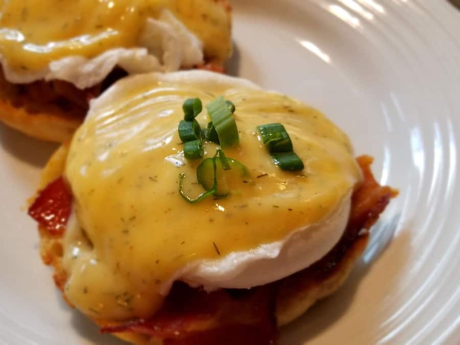 A plate with two eggs benedict sandwiches topped with hollandaise sauce and garnished with chives.