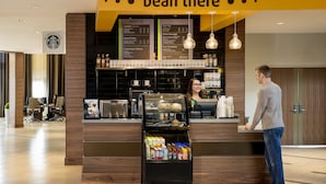 Una cafetería Starbucks con un menú, un refrigerador con bebidas y un mostrador con cajero.