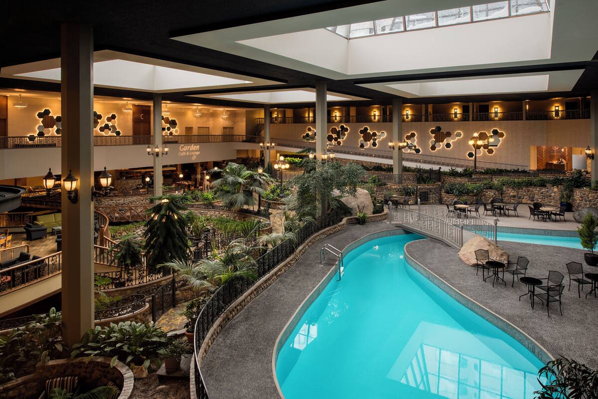 A multi-level indoor pool area with a central pool, surrounded by seating areas and greenery.
