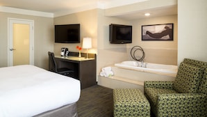 Habitación de hotel con cama, escritorio, silla, televisor y baño con bañera e inodoro.