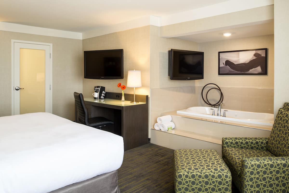 A hotel room with a bed, desk, chair, TV, and a bathroom with a bathtub and toilet.