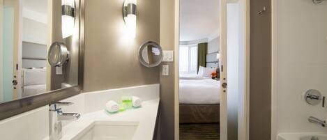 Une salle de bain d’hôtel avec un grand miroir, un lavabo, une baignoire et une douche.