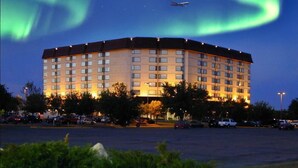 Un hotel de varios pisos con techo plano, rodeado de un estacionamiento y zonas verdes.