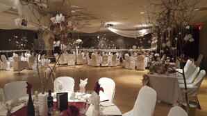 A banquet hall with round tables and white chairs, decorated with floral arrangements and string lights. - Hôtel des Eskers (Amos)