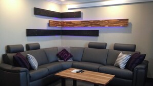 A modern living room with a sectional sofa, a wooden coffee table, and built-in shelving with a blue backlight. - Hôtel des Eskers (Amos)