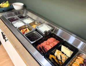 A buffet with various food items including sliced tomatoes, cheese, and fruits. - Hôtel des Eskers (Amos)