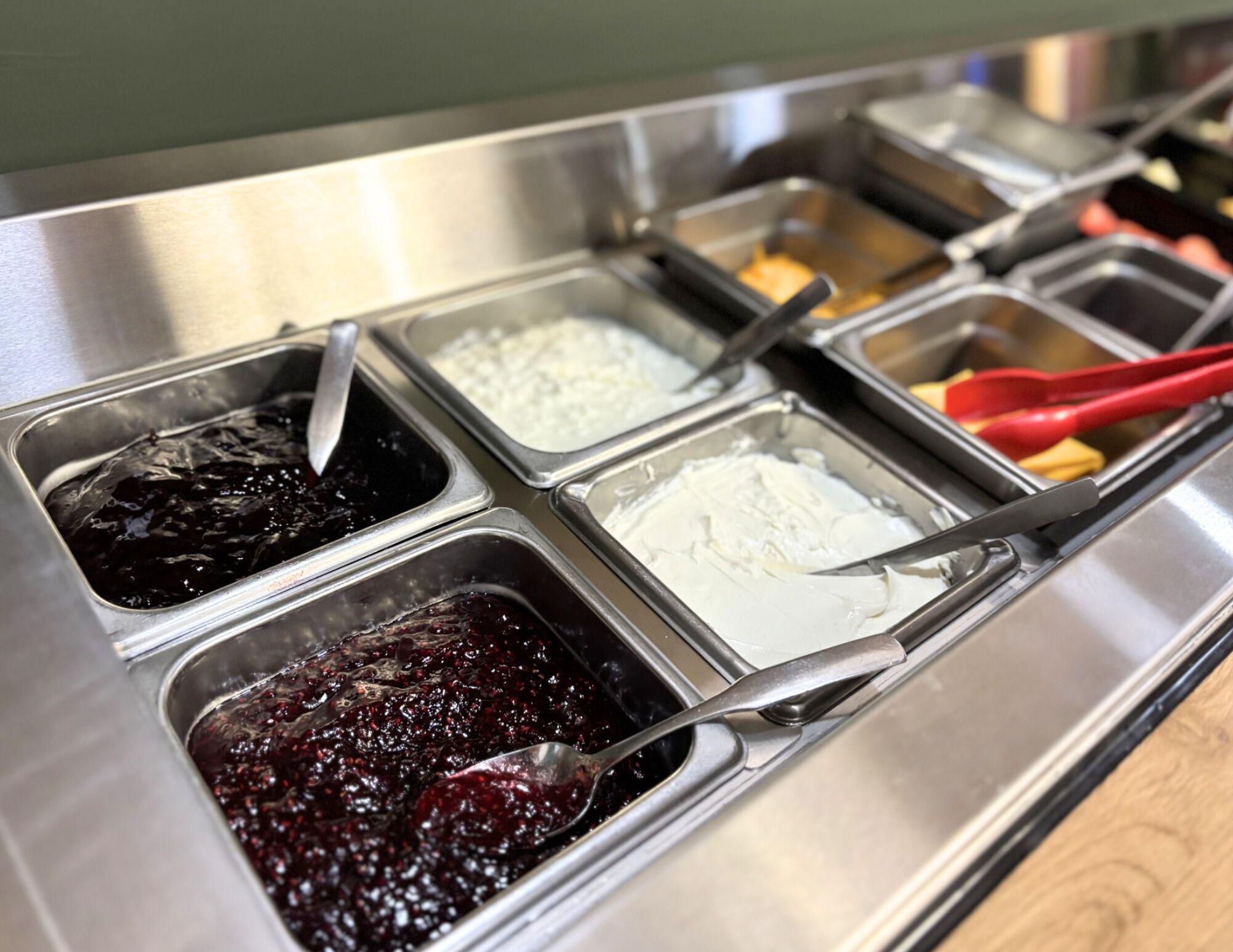 A buffet with multiple food containers including a dark red fruit compote, white cream, and a yellow sauce.