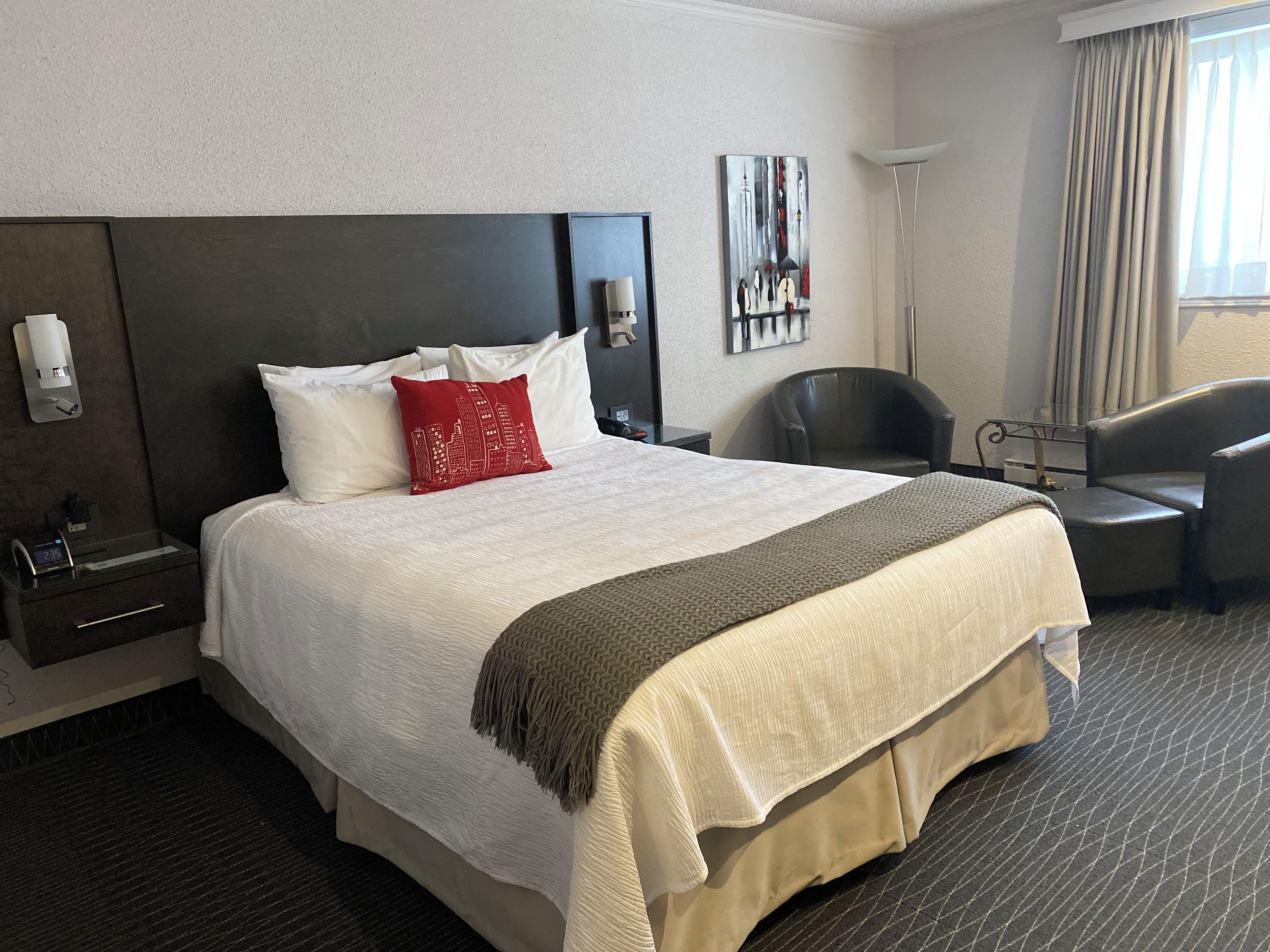 A hotel room with a large bed, a desk, a chair, a painting on the wall, and a window with curtains.