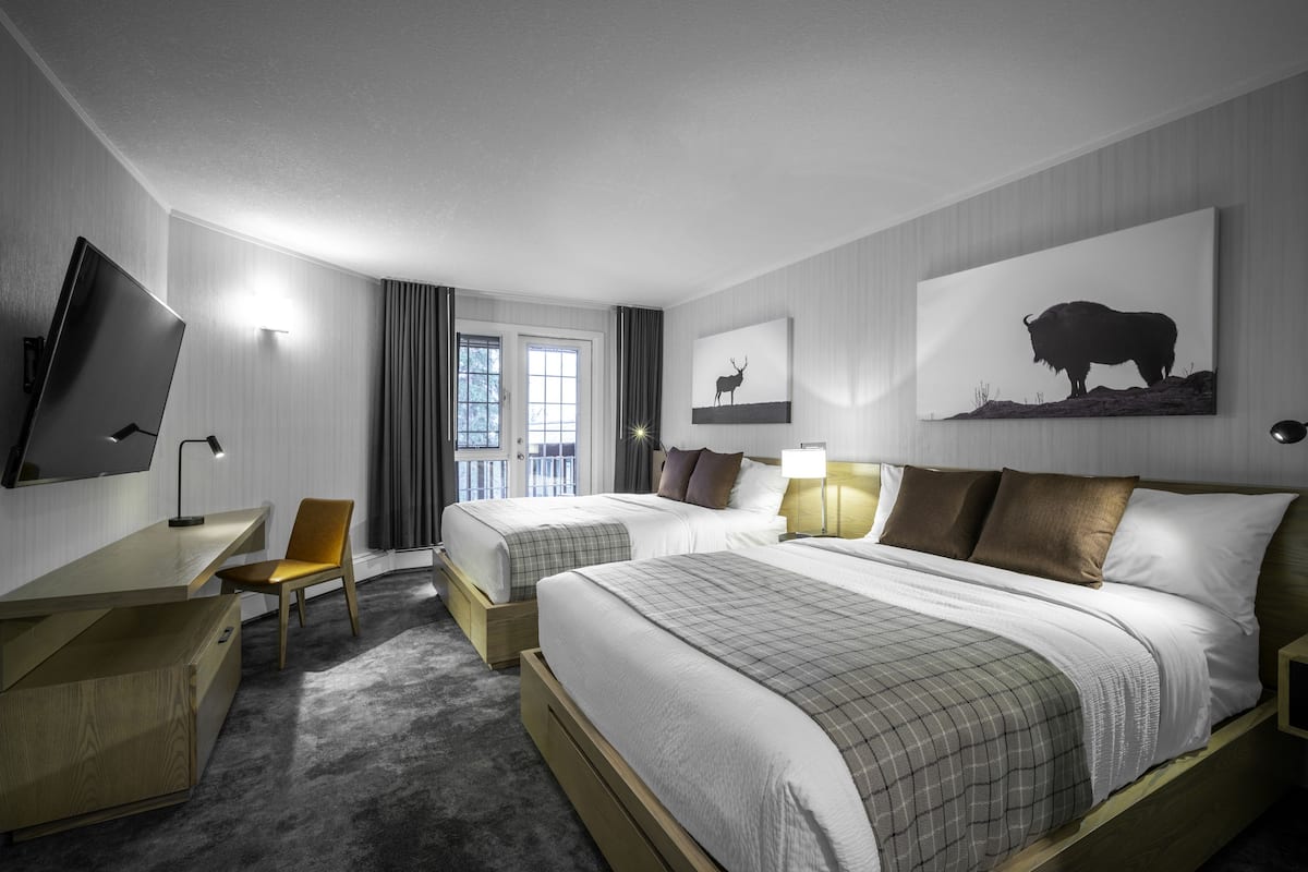 A hotel room with two beds, a desk, a chair, a TV, and artwork on the walls.