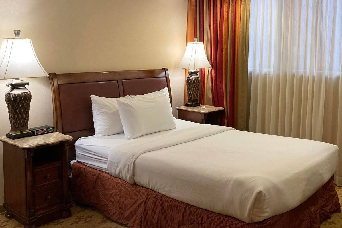 A hotel room with a large bed, two bedside tables with lamps, a wooden headboard, and a patterned carpet.