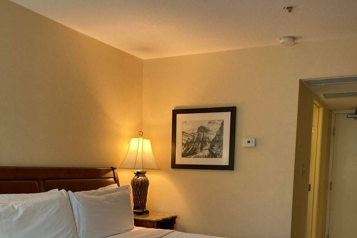 A hotel room with a large bed, a bedside lamp, a framed picture on the wall, and a door to the right.