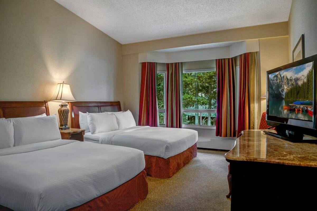 A hotel room with two beds, a television, and a window with curtains.