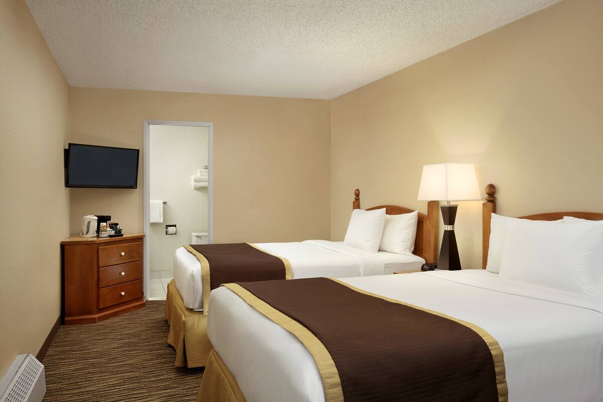 A hotel room with two beds, a TV, a desk with a coffee maker, and a lamp.