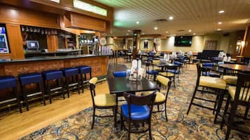 Un comedor de hotel con bar, varias mesas y sillas, y suelo alfombrado.