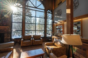 A cozy living room with leather sofas, a fireplace, and large windows offering a view of snow-covered trees.