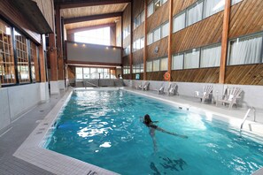 An indoor swimming pool with a wooden interior, clear water, and a lifeguard chair.