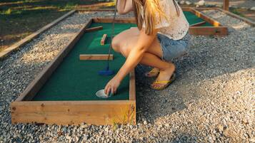 A person playing mini-golf in a courtyard with wooden buildings in the background.