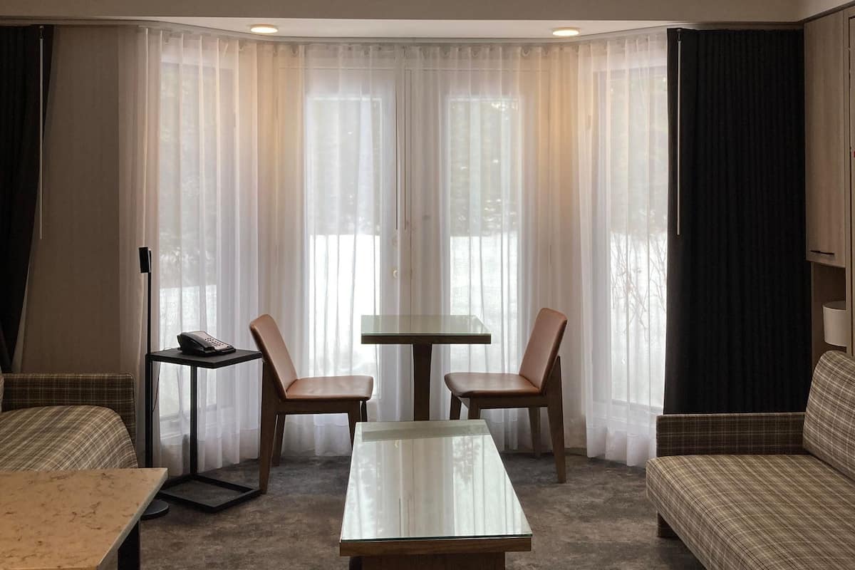 A hotel room with a sofa, a small table, two chairs, a desk, and a telephone.
