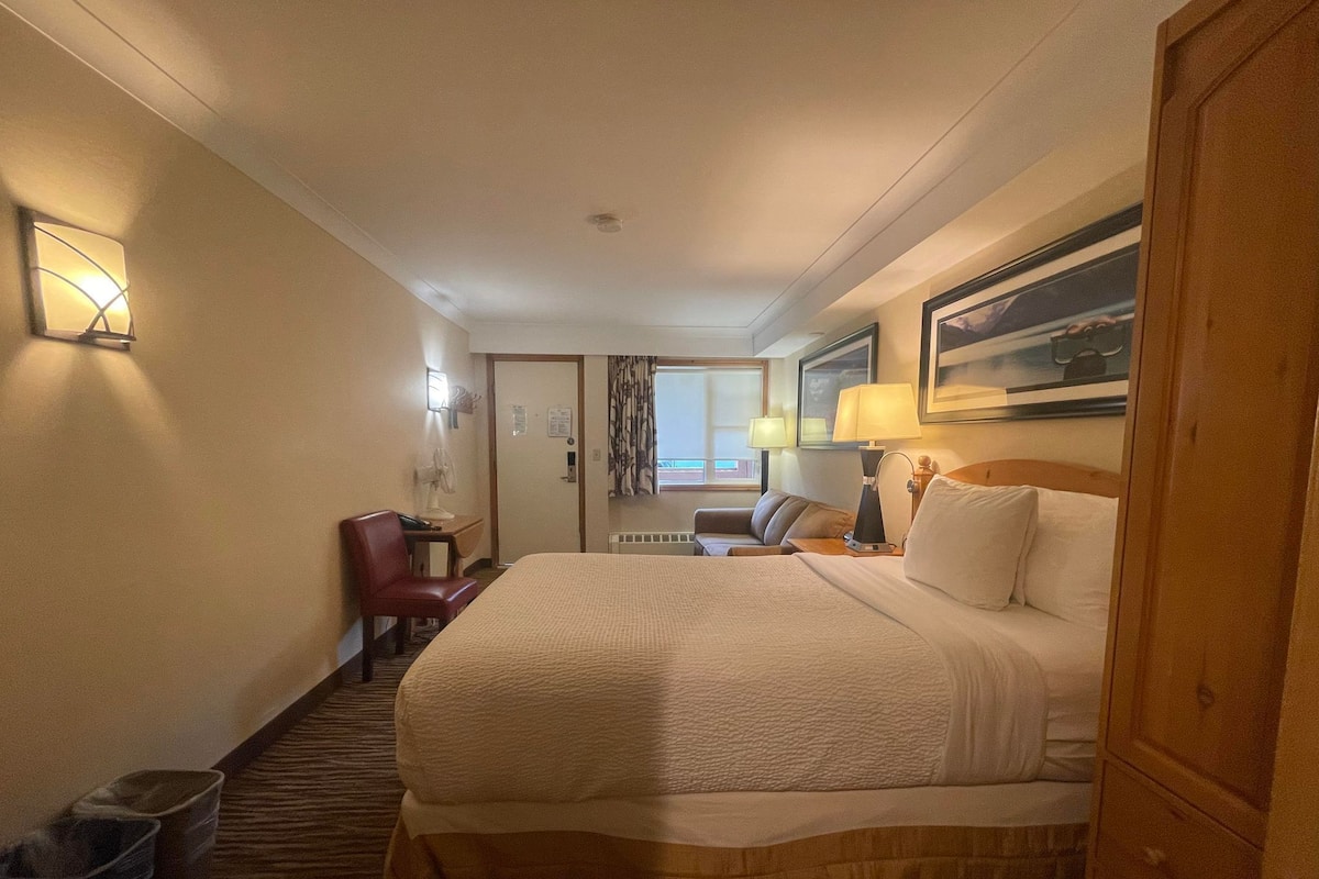 A hotel room with a large bed, a desk, a chair, and a window with curtains.