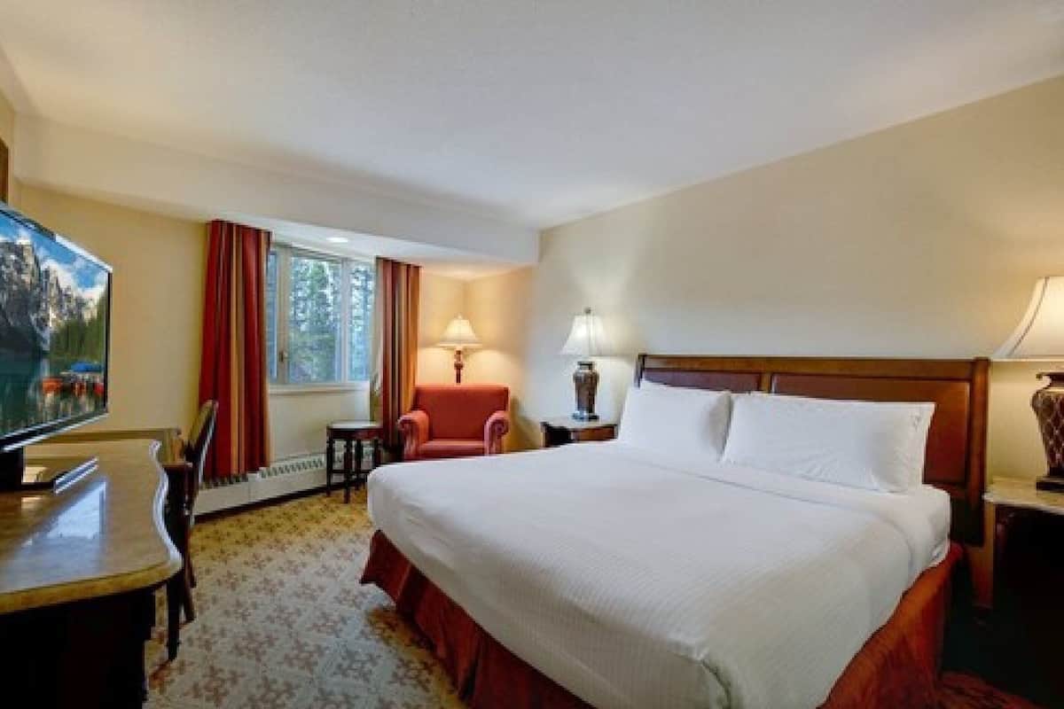 A hotel room with a bed, a TV, a desk, a chair, and a window with curtains.