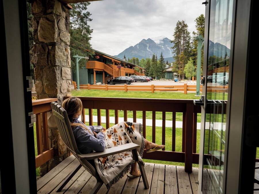 A wooden deck with a stone pillar, a bench, and a view of a mountain range.