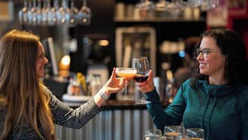 Dos personas brindando con bebidas en un bar, con una pizza sobre la mesa.