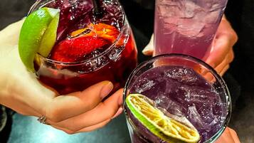 Three glasses of beverages with lime slices and a strawberry, held by hands.