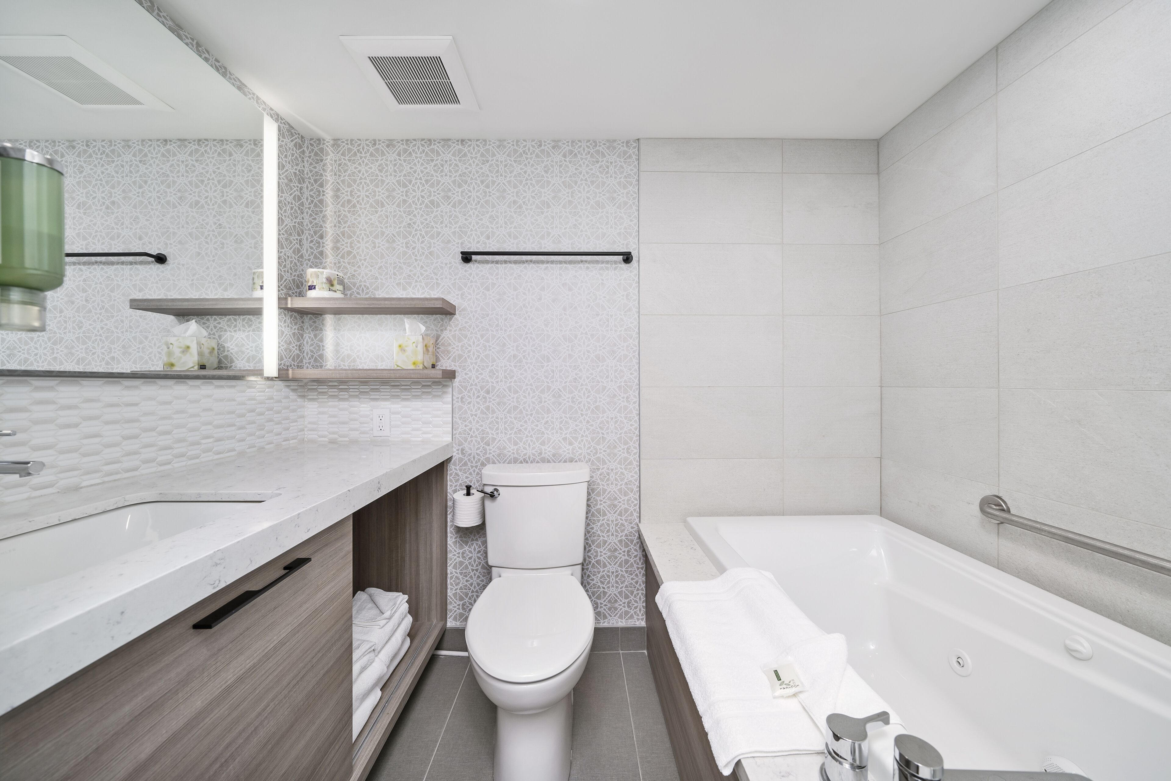A modern bathroom with a white sink, toilet, and bathtub. There are shelves with toiletries and a towel rack.