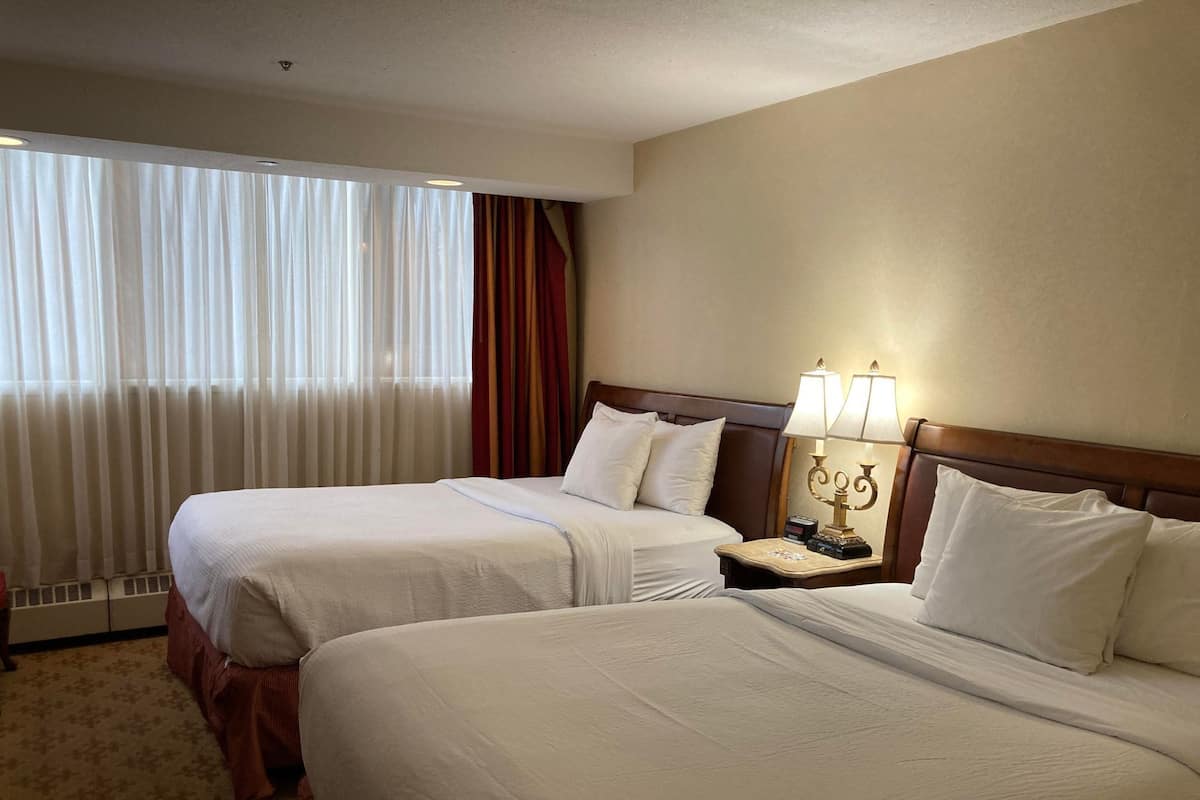 A hotel room with two beds, a nightstand with a lamp, and a window with curtains.