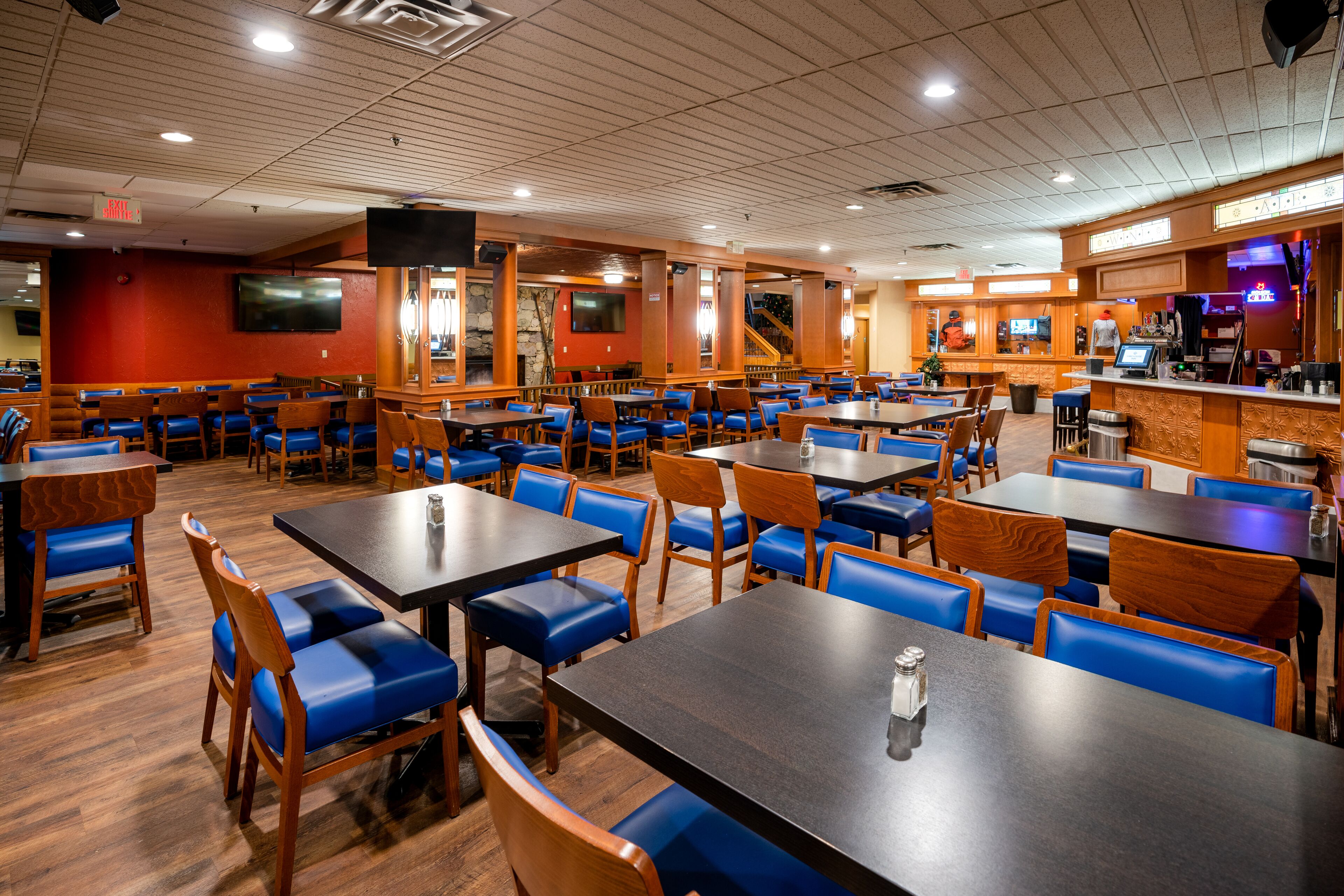 A restaurant with multiple tables and booths, wooden flooring, and a bar area.