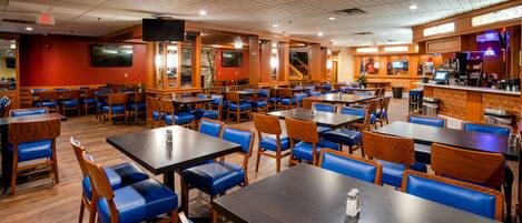 A restaurant with multiple tables and booths, wooden flooring, and a bar area.