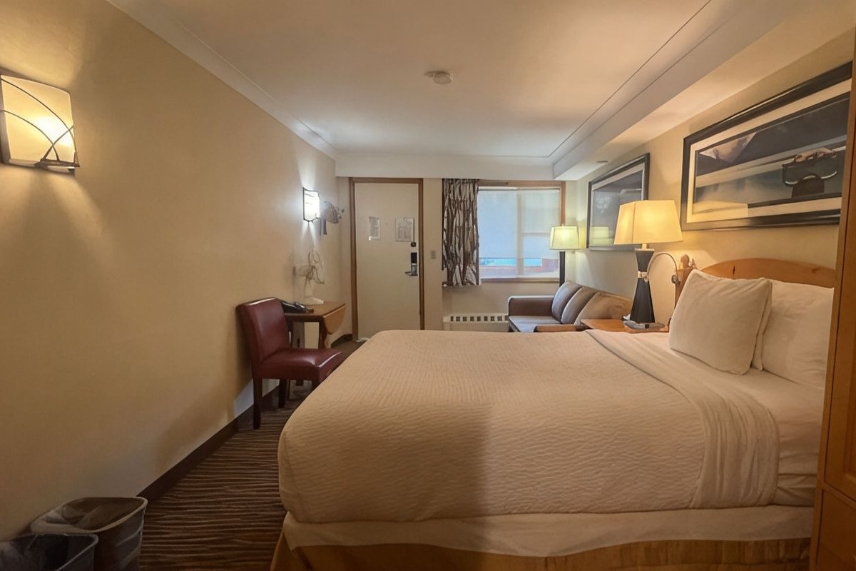 A hotel room with a large bed, a desk with a chair, a window with curtains, and a painting on the wall.